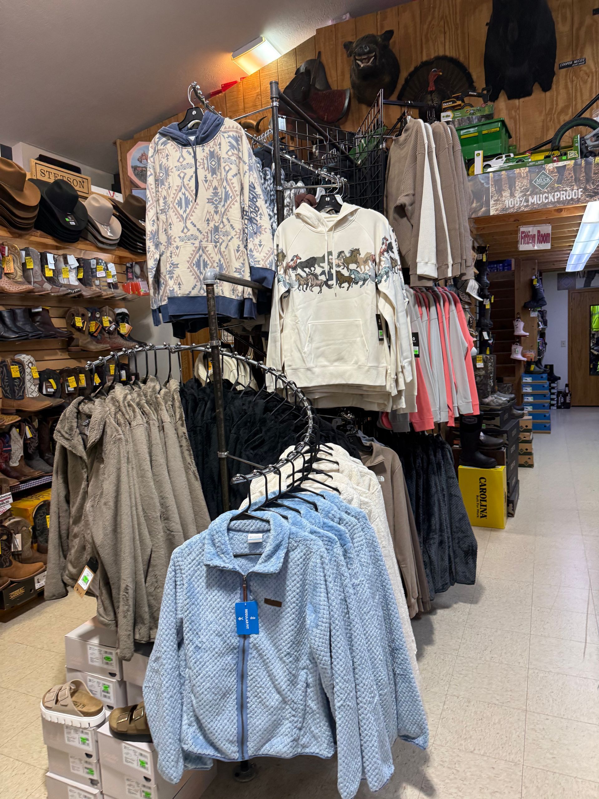 Clothing store aisle with racks of hanging shirts, jackets, and pants in a small shop