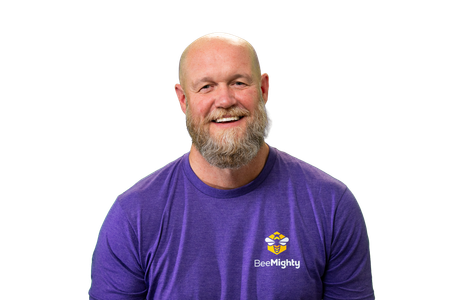 Man with a bald head and beard wearing a purple shirt, smiling against a white background.