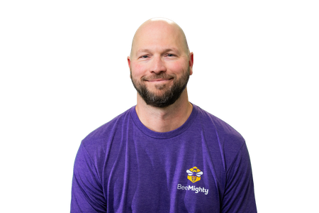 Man with a bald head and beard wearing a purple shirt, smiling, against a white background.