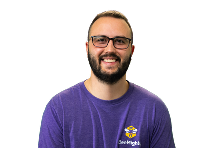 Man with a beard and glasses smiling, wearing a purple shirt with a logo on a white background.