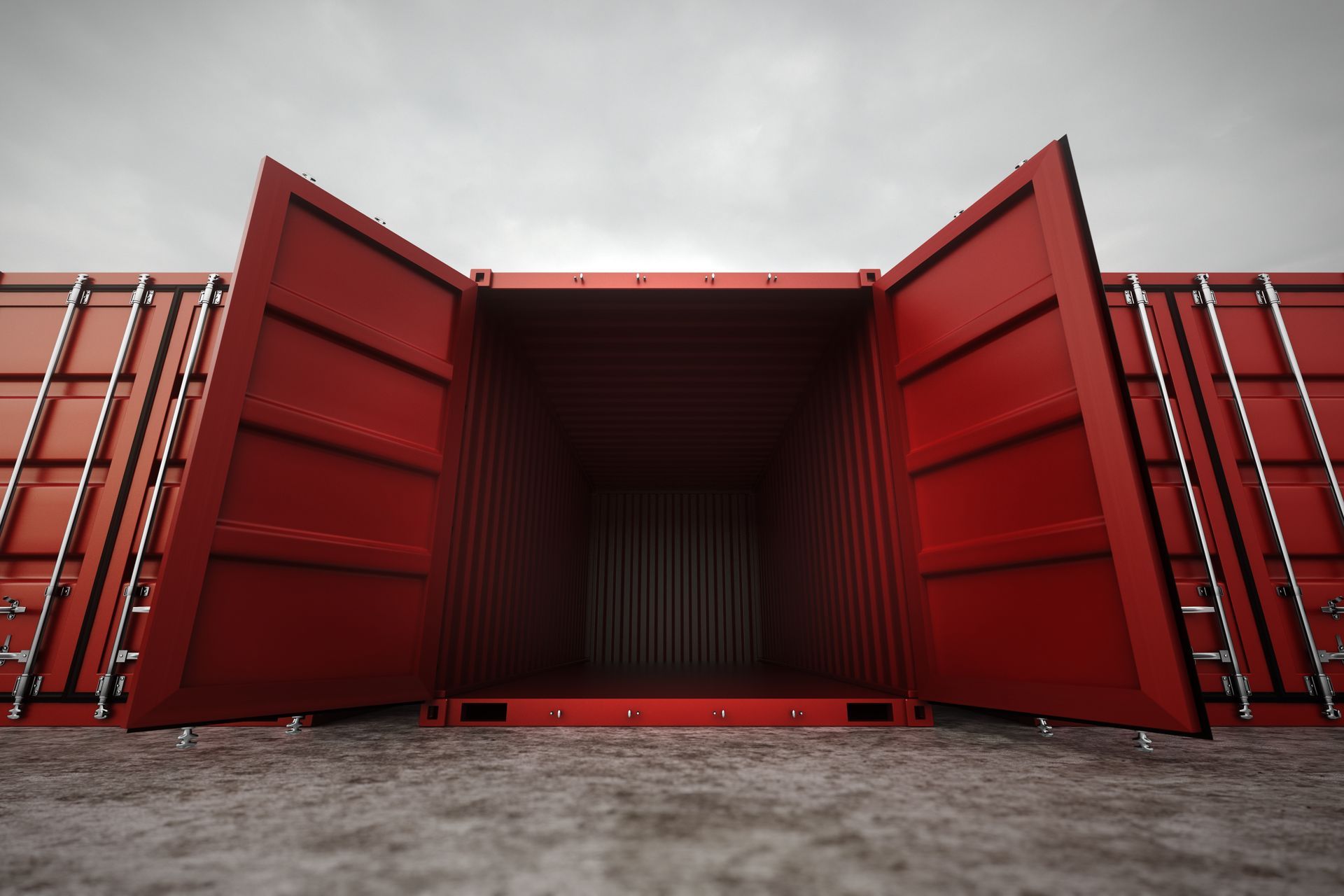 An open, empty red shipping container sits on a flat, gray surface under an overcast sky.