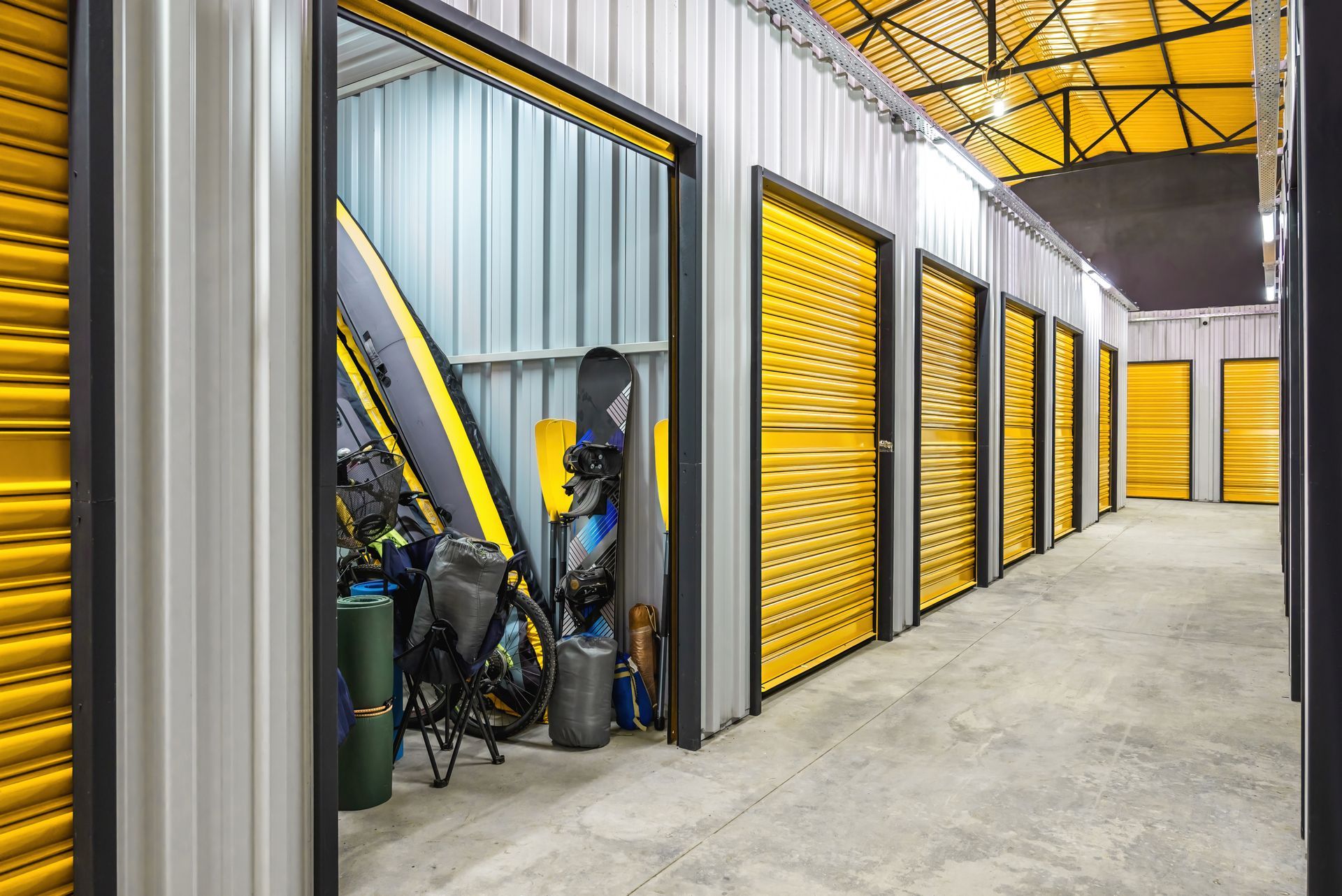 Storage units with yellow doors and various items stored in one open unit.