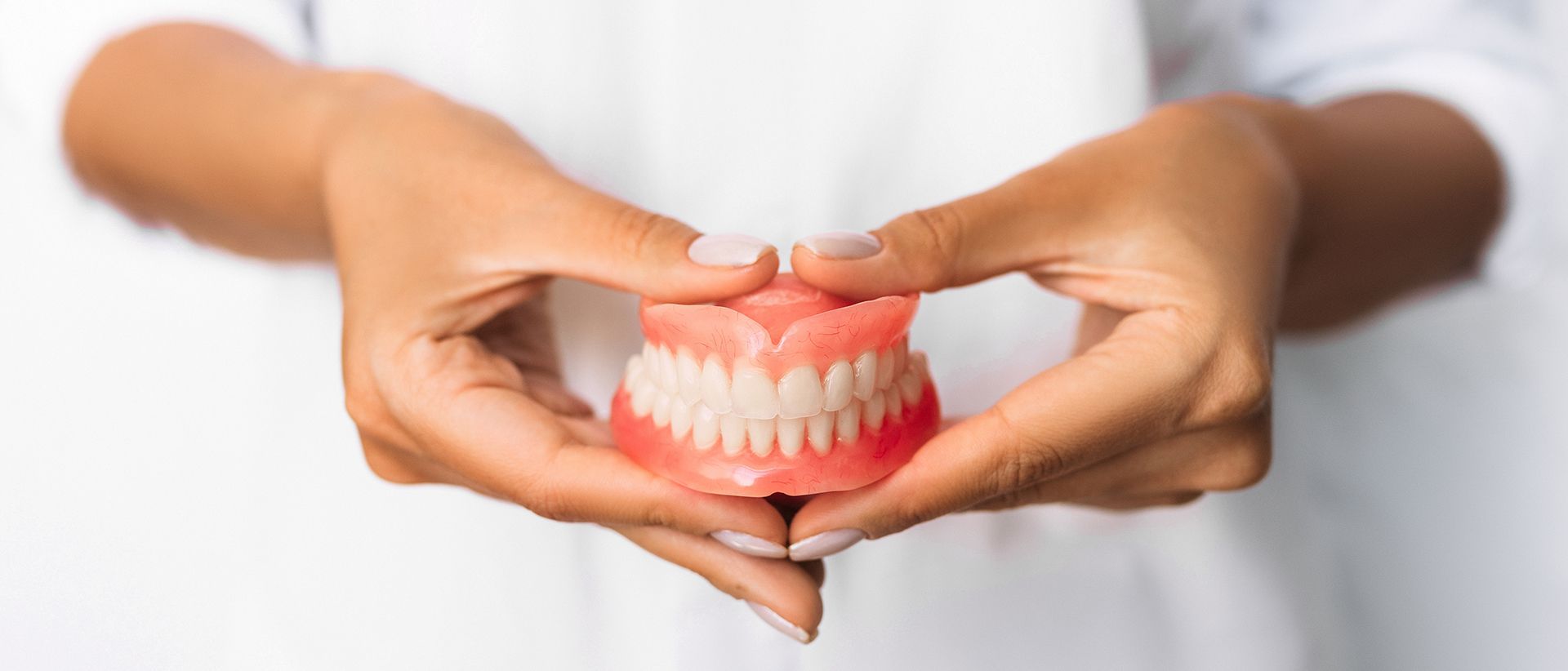 A Woman Is Holding a Denture in Her Hands in The Shape of A Heart — Buderim Denture Studio In Buderim, QLD