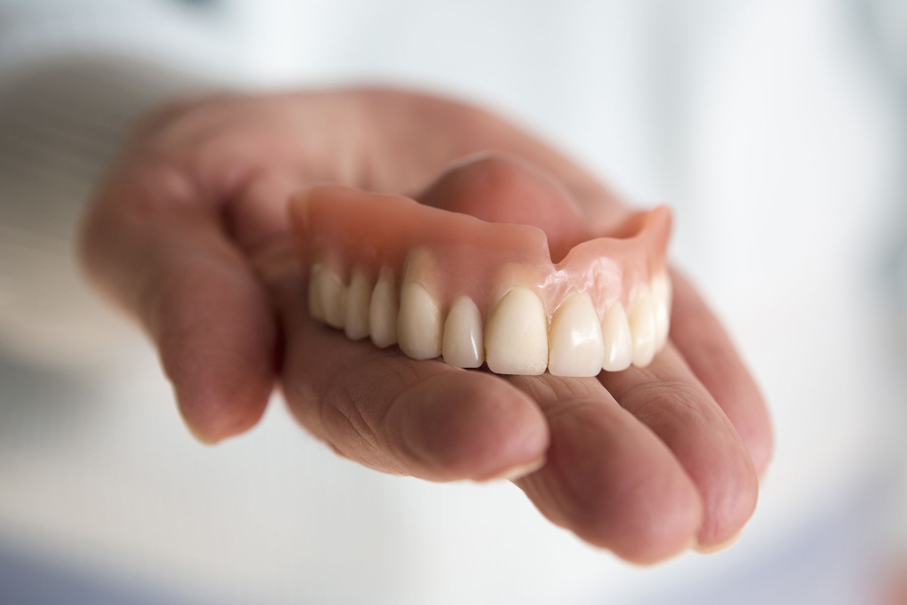 A Person Is Holding a Full Denture in Their Hand — Buderim Denture Studio In Buderim, QLD