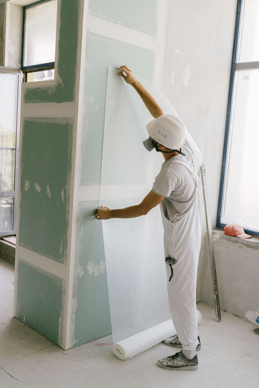 Worker applying drywall compound to a wall inside a room under renovation
