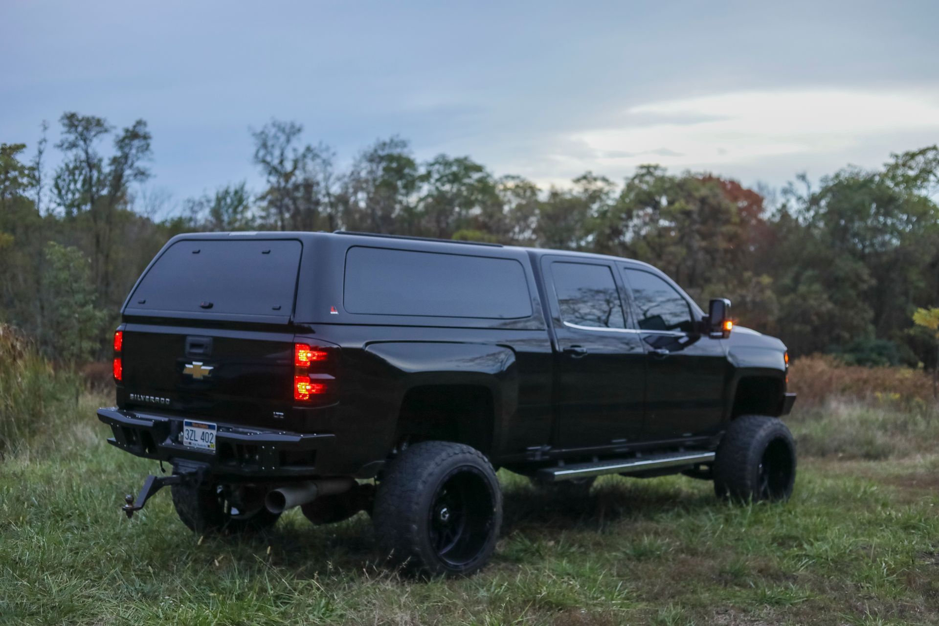 A black truck with a canopy is parked in a grassy field.