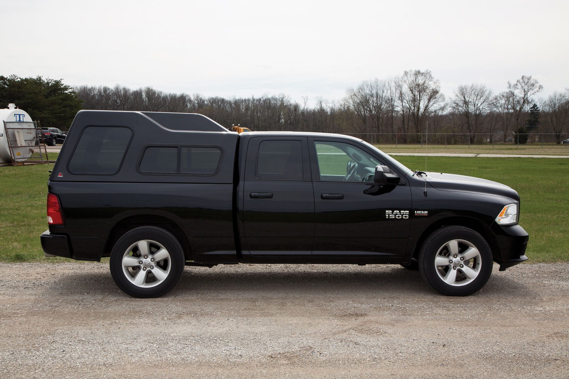 A black truck with a canopy on top of it is parked in a gravel lot.