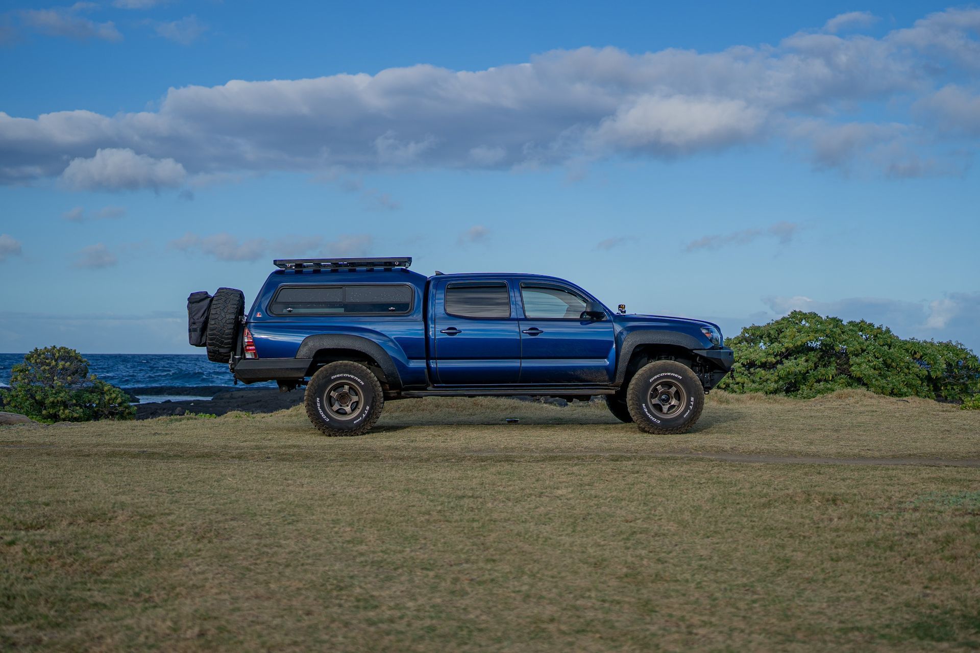 A blue truck is parked in a grassy field near the ocean.
