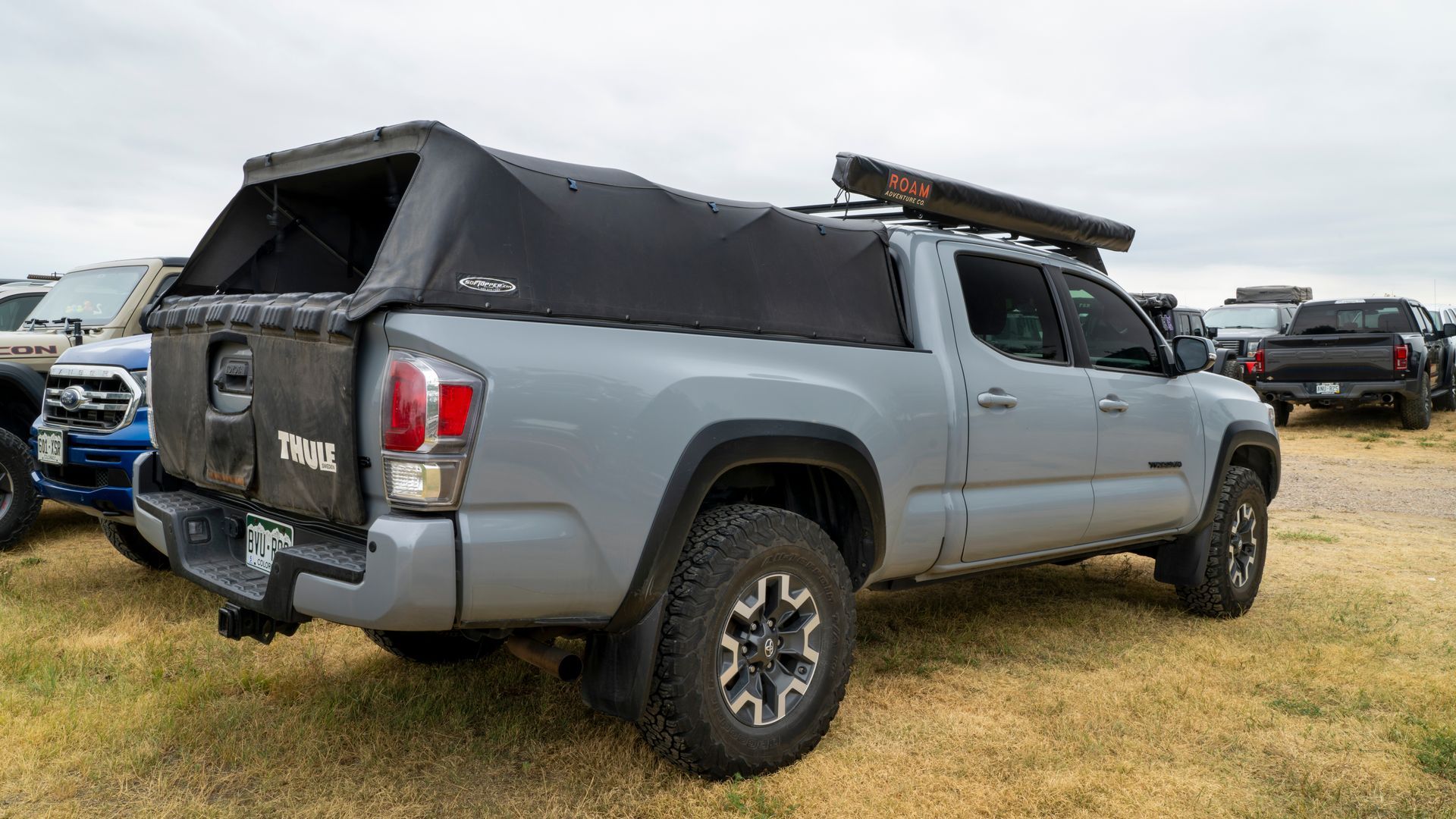 Gray pickup truck with black camper shell parked on grass at an outdoor event