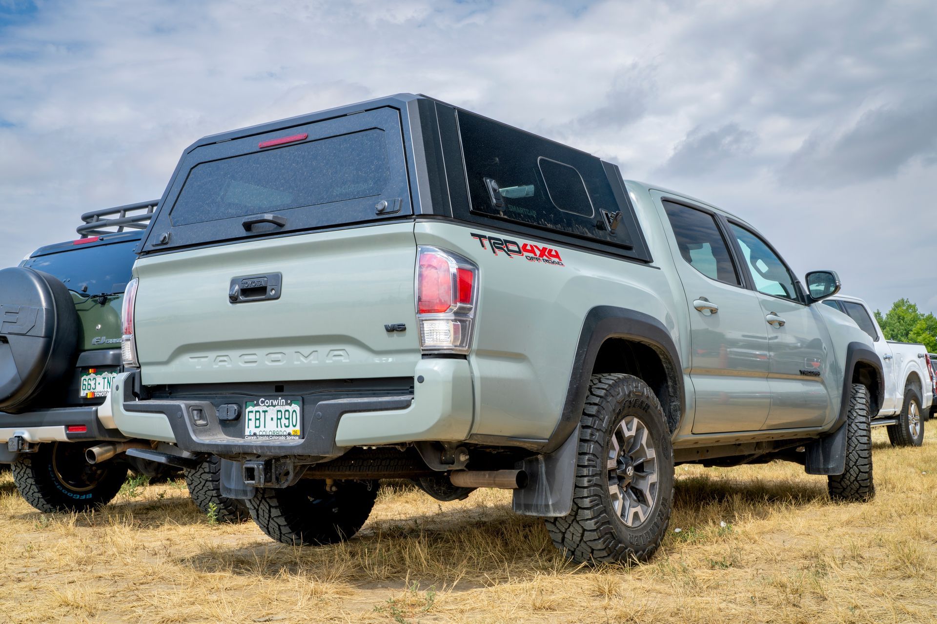 Two gray Toyota Tacoma pickup trucks parked on dry grass under a cloudy sky
