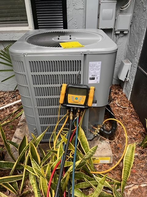Outdoor air conditioner unit with yellow multimeter and tangled red/black wires in front of a house