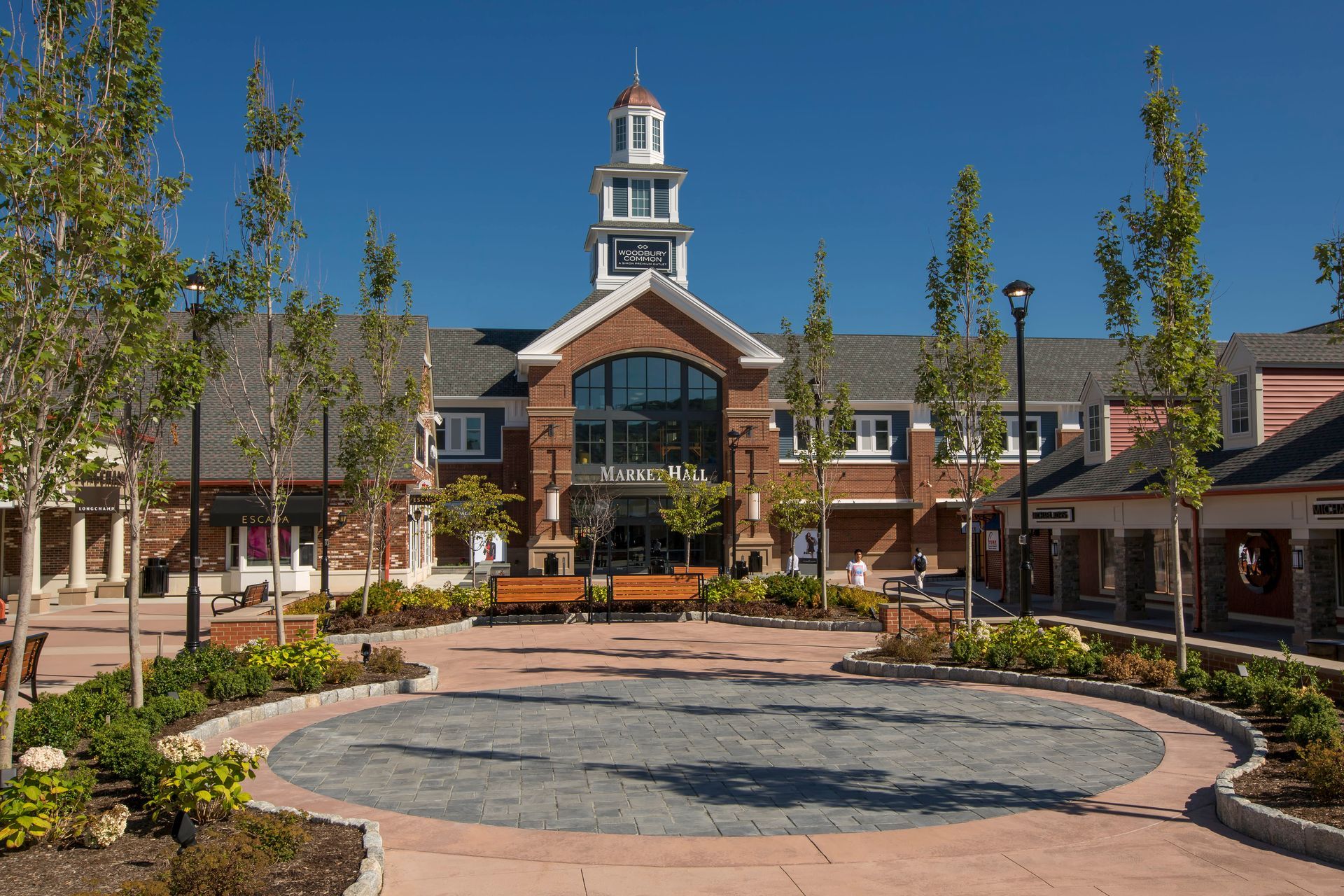 Courtyard with circular stone fountain, brick buildings, and a central cupola under a clear blue sky