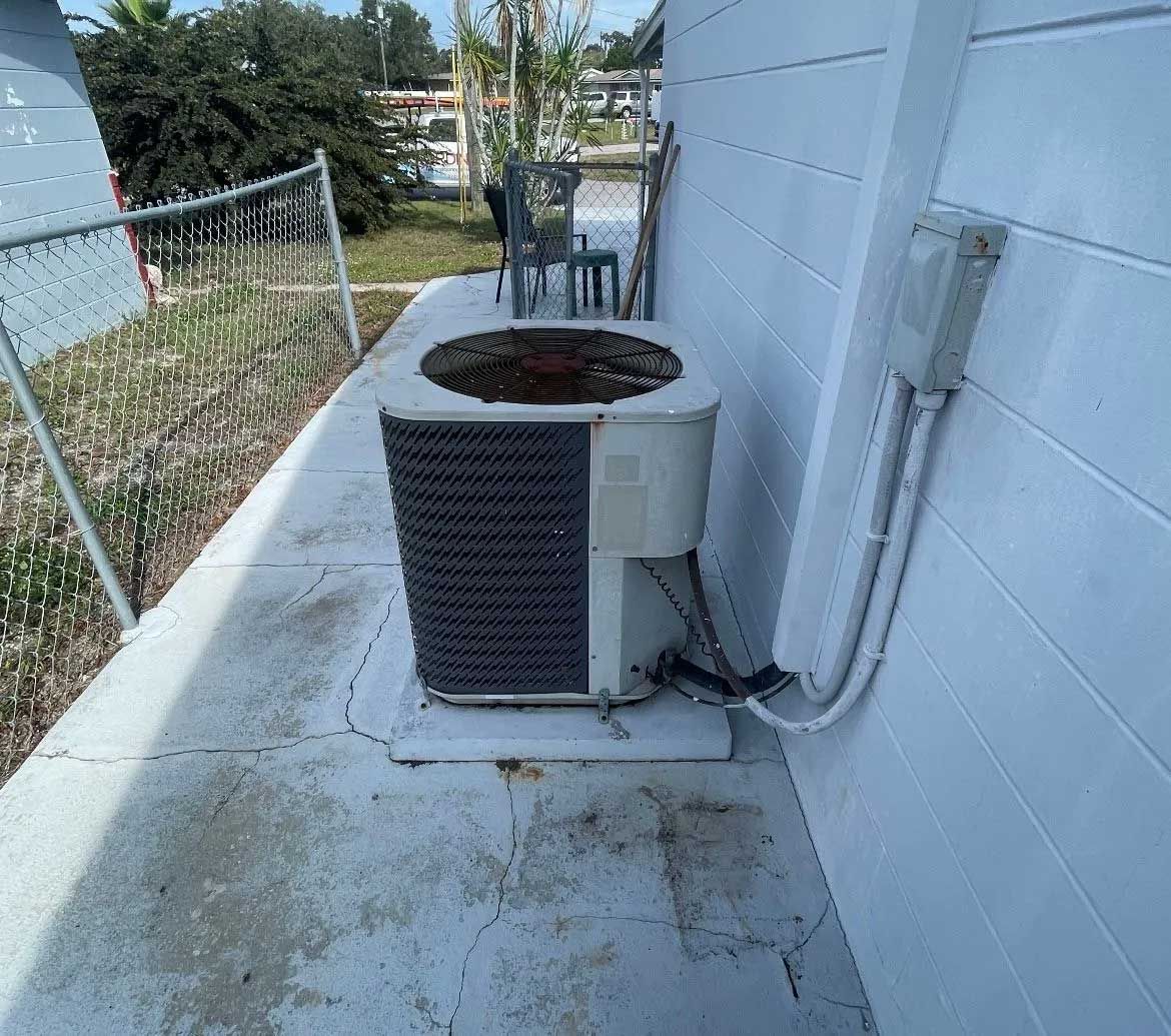 Outdoor HVAC unit beside a white house wall along a concrete side yard path