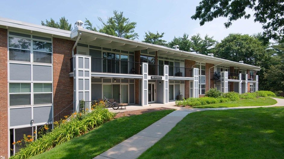 Brick apartment building with balconies, large windows, and a grassy walkway in front