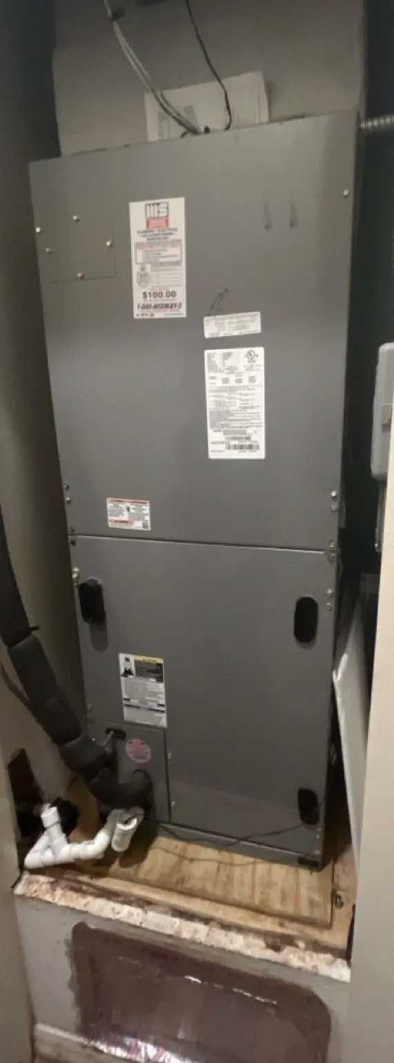 Gray HVAC furnace in a utility closet with pipes and labels, viewed from the front with access panels visible