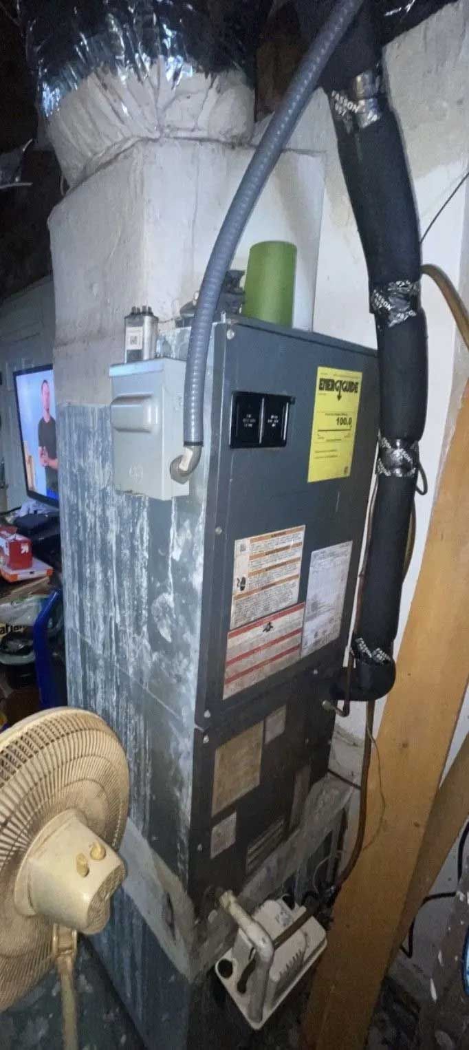 Electrical control panel with wiring and pipes mounted beside a large cylindrical tank in an industrial room