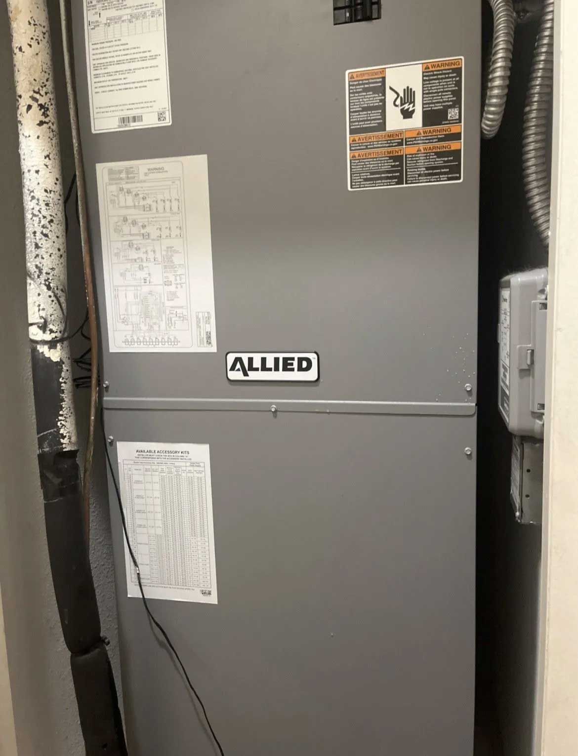 Gray Allied furnace in a utility closet with papers taped to the front and ductwork on the right