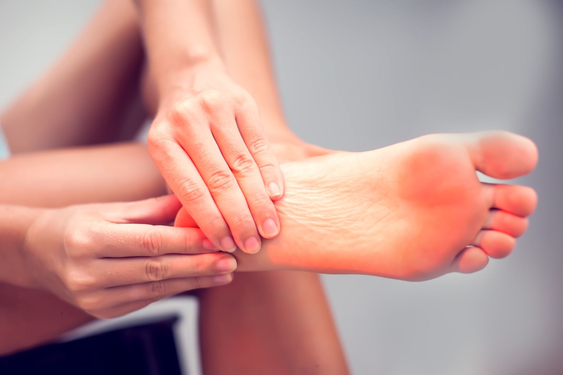 Person touching their foot, highlighting the arch, with a red area indicating pain.