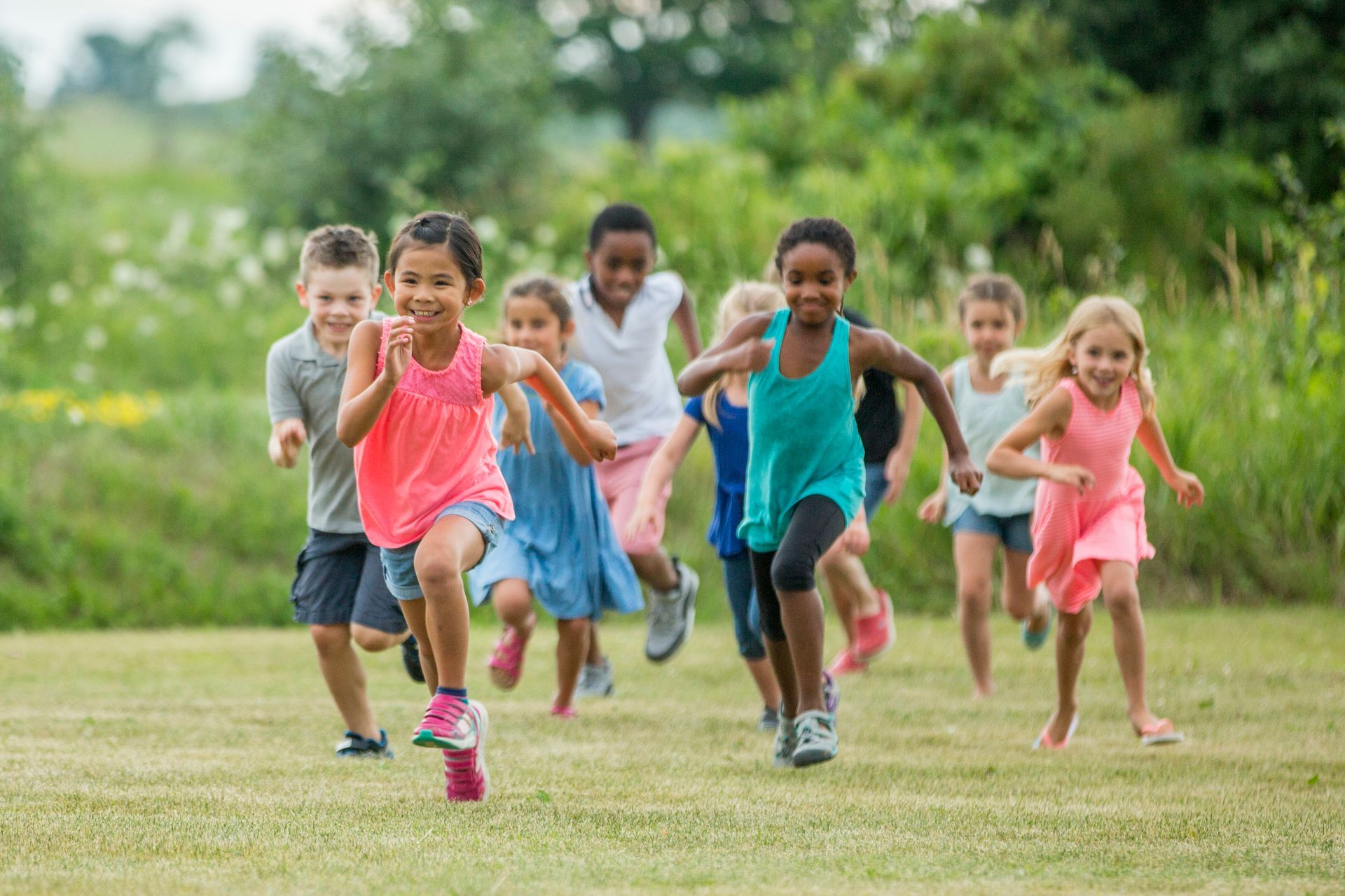 Children running on a grassy field; several wear colorful clothing, with joyful expressions.