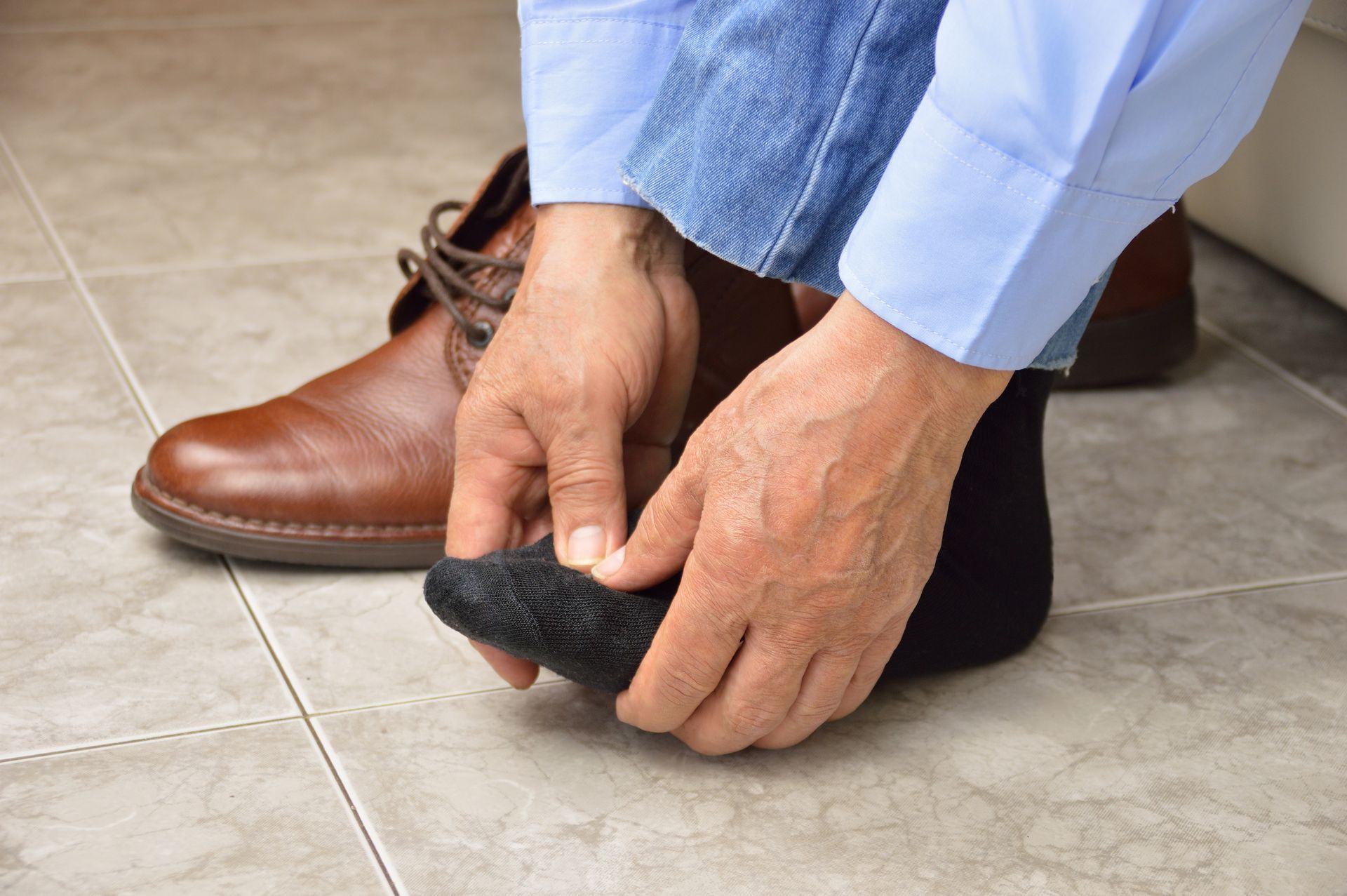 Person putting on a black sock. Brown shoe on the floor nearby.