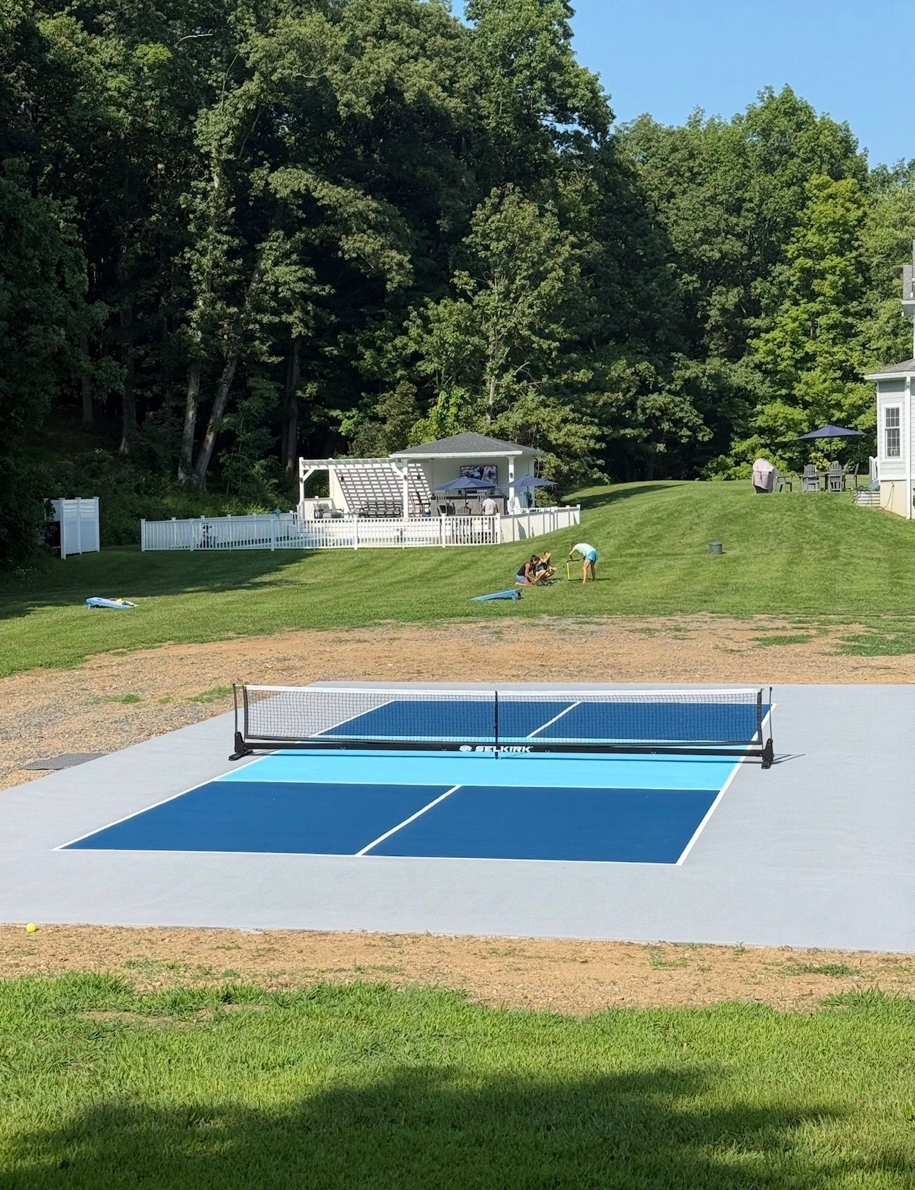 Outdoor blue ping-pong table on a concrete pad in a grassy backyard with trees and a patio in the background