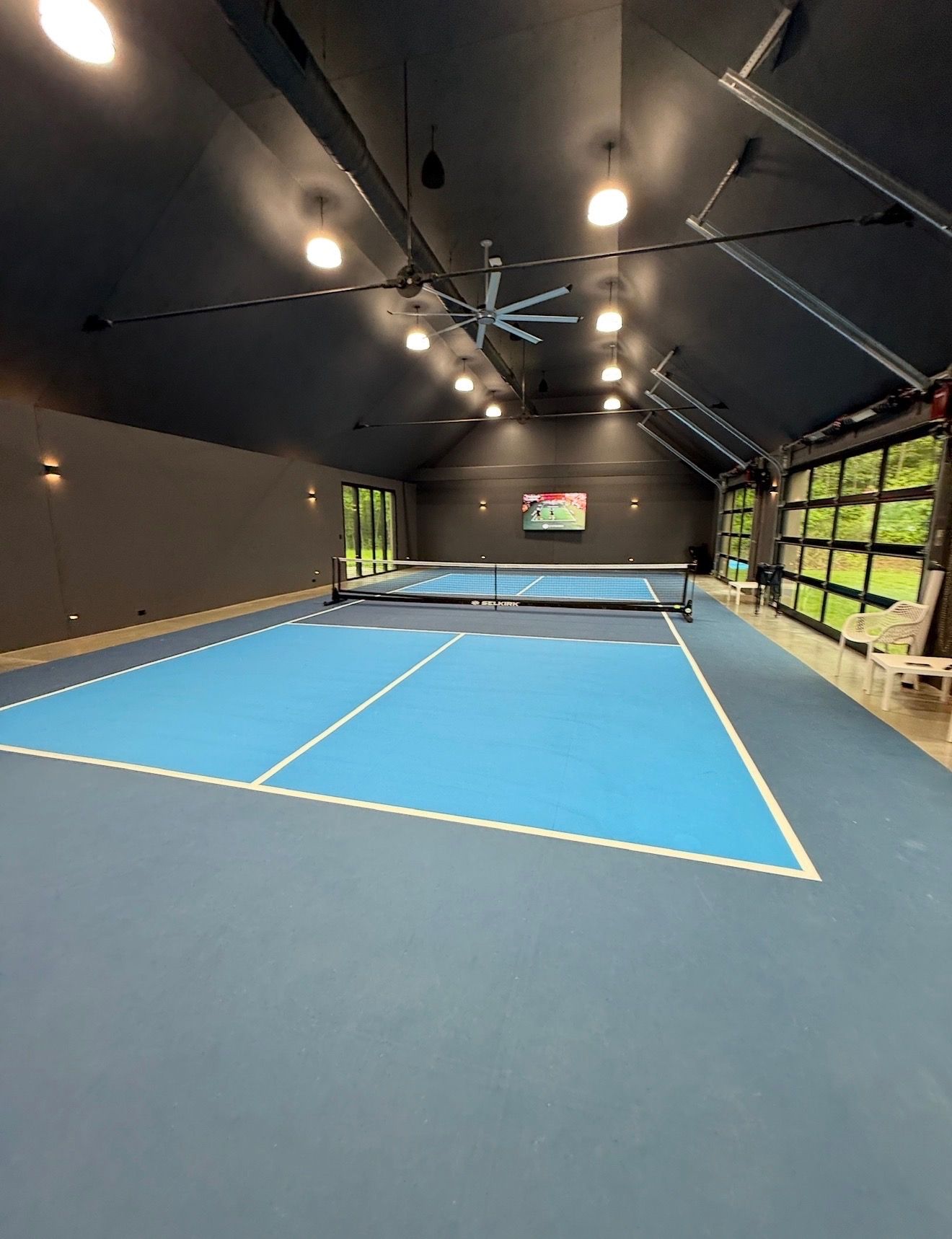 Indoor tennis court with blue playing surface, dark ceiling, and bright lights inside a tent-like enclosure