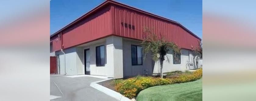 Red-roofed commercial building with white walls, a sidewalk, and landscaping under a clear blue sky