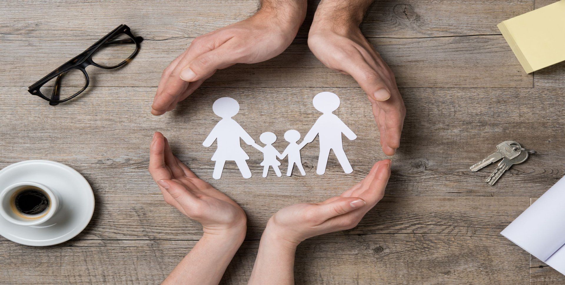 Hands cupping a paper cutout family; concept of care, protection, and insurance.