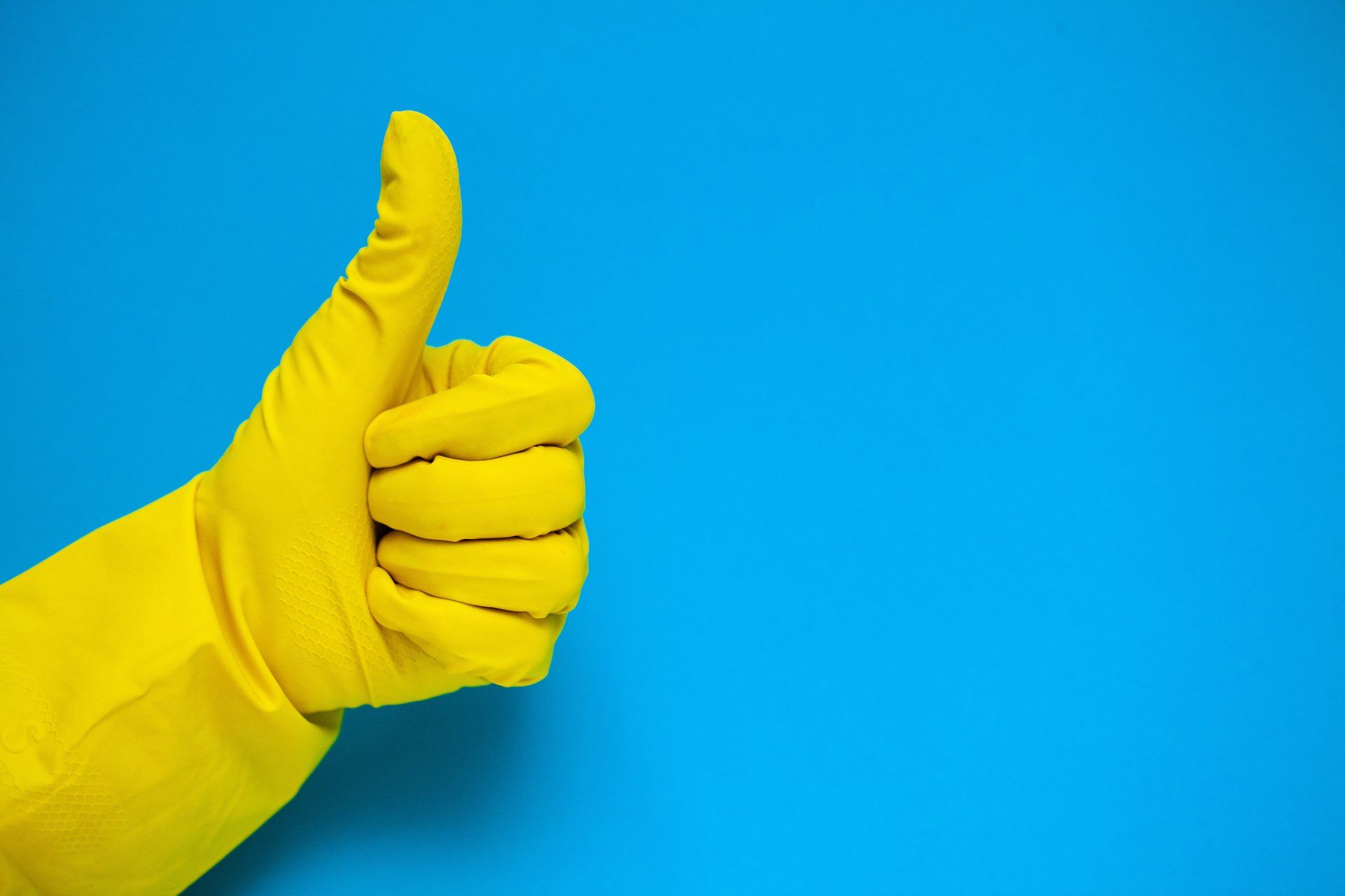 Un gant en caoutchouc jaune fait un signe de pouce levé sur un fond bleu.