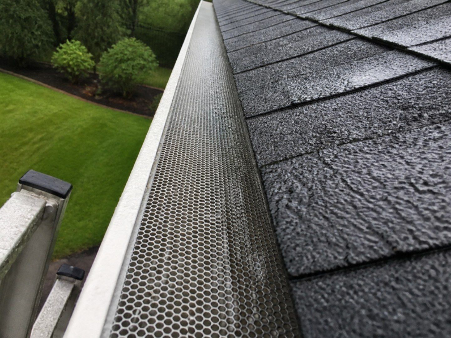 Rain passing through a micro-mesh gutter guard along a wet shingle roof