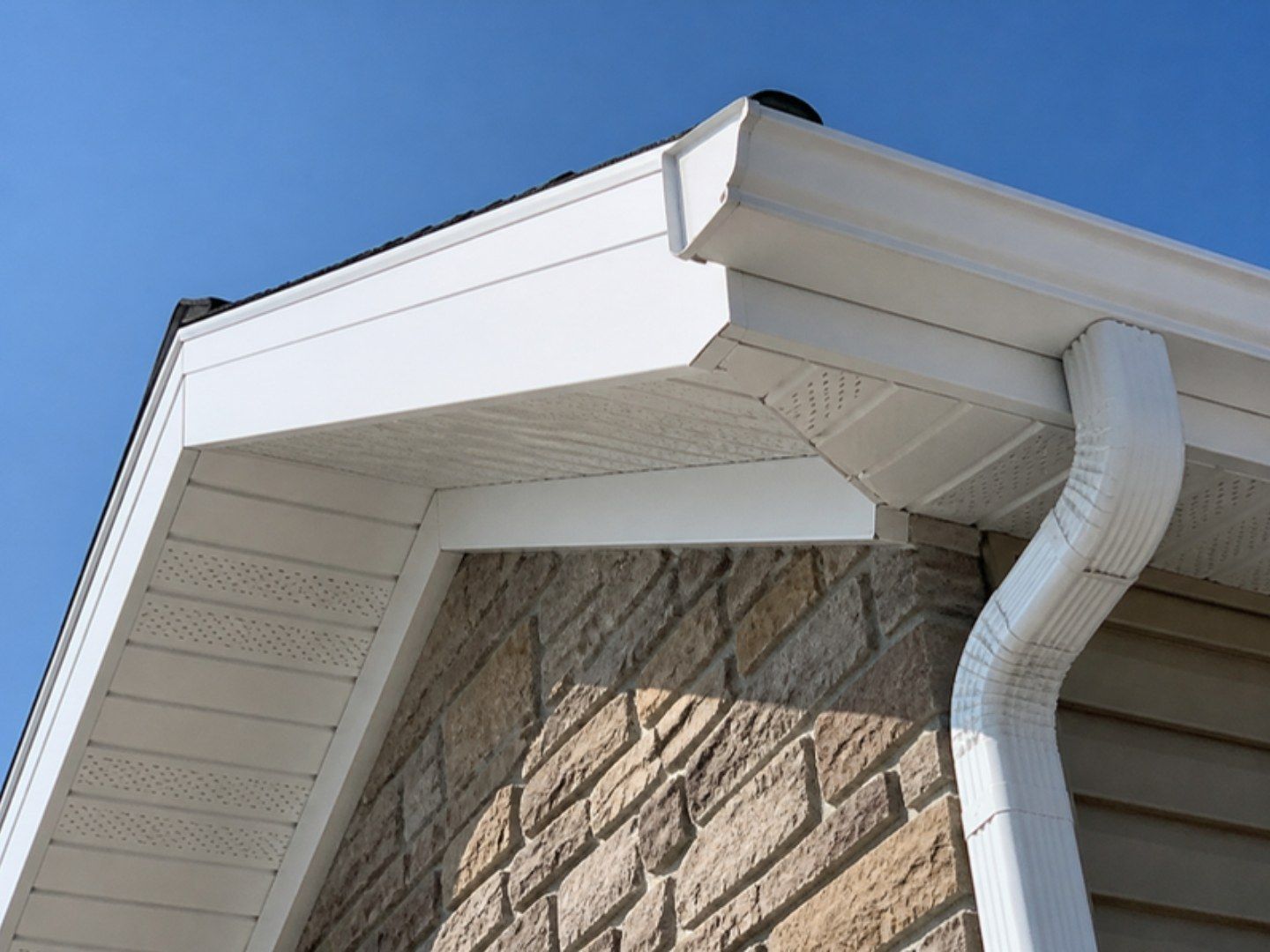 House eave corner with white fascia, vented soffit, and gutter after repair