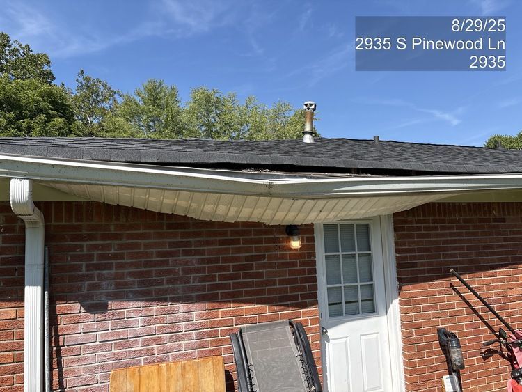 Brick house exterior with white door, window, gutter, and rooftop; roof appears damaged near the ridge.