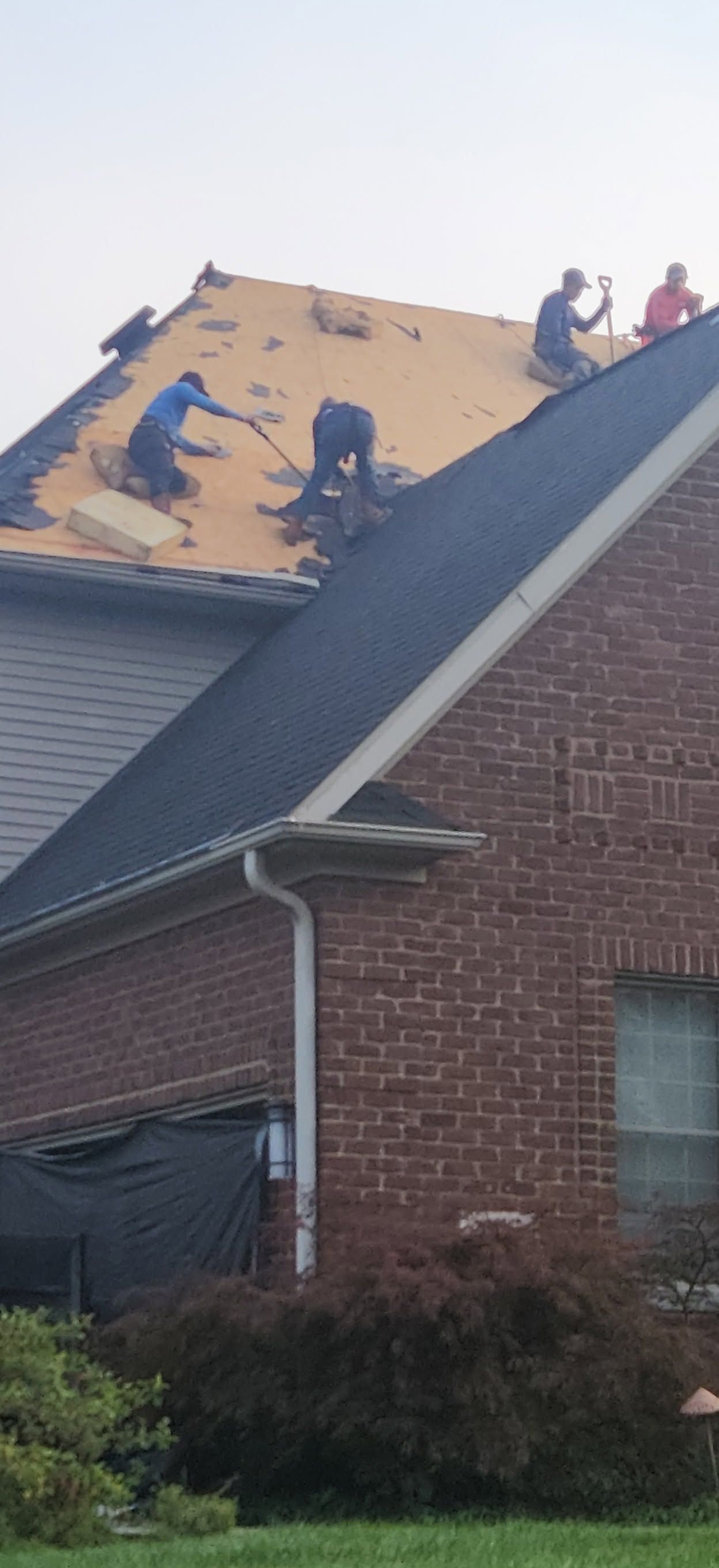 Roofers working on a yellow house roof with exposed underlayment and scattered shingles