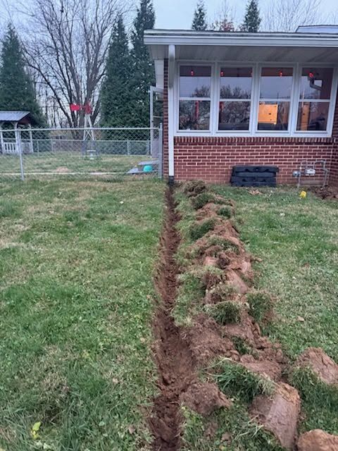 Trench dug beside a house, with overturned soil along a grassy yard at dusk.
