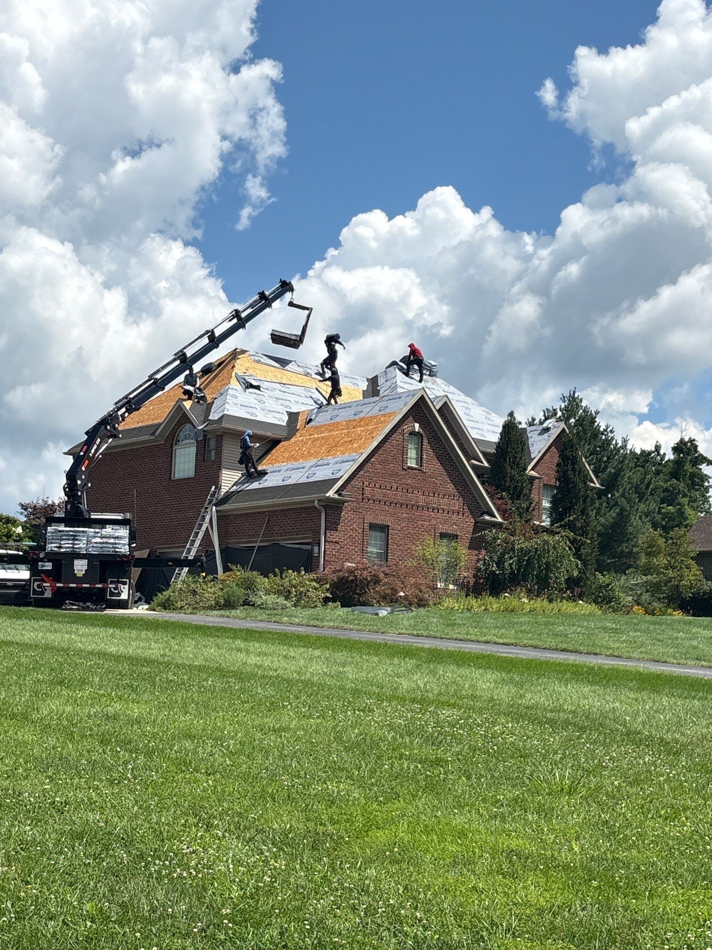 Workers repairing a house roof with a crane amid storm damage under a cloudy sky
