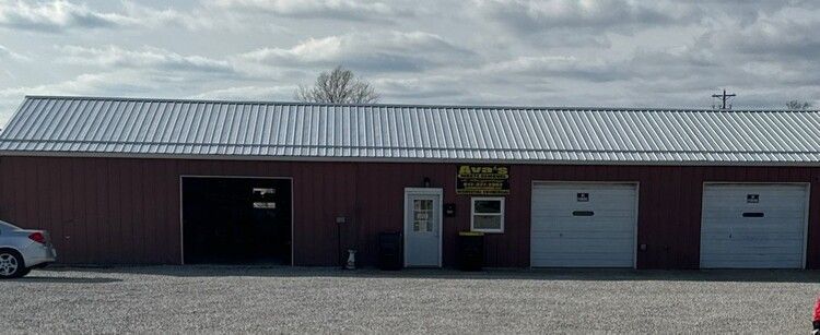 Red metal commercial building with garage doors and a small central entrance on a gravel lot