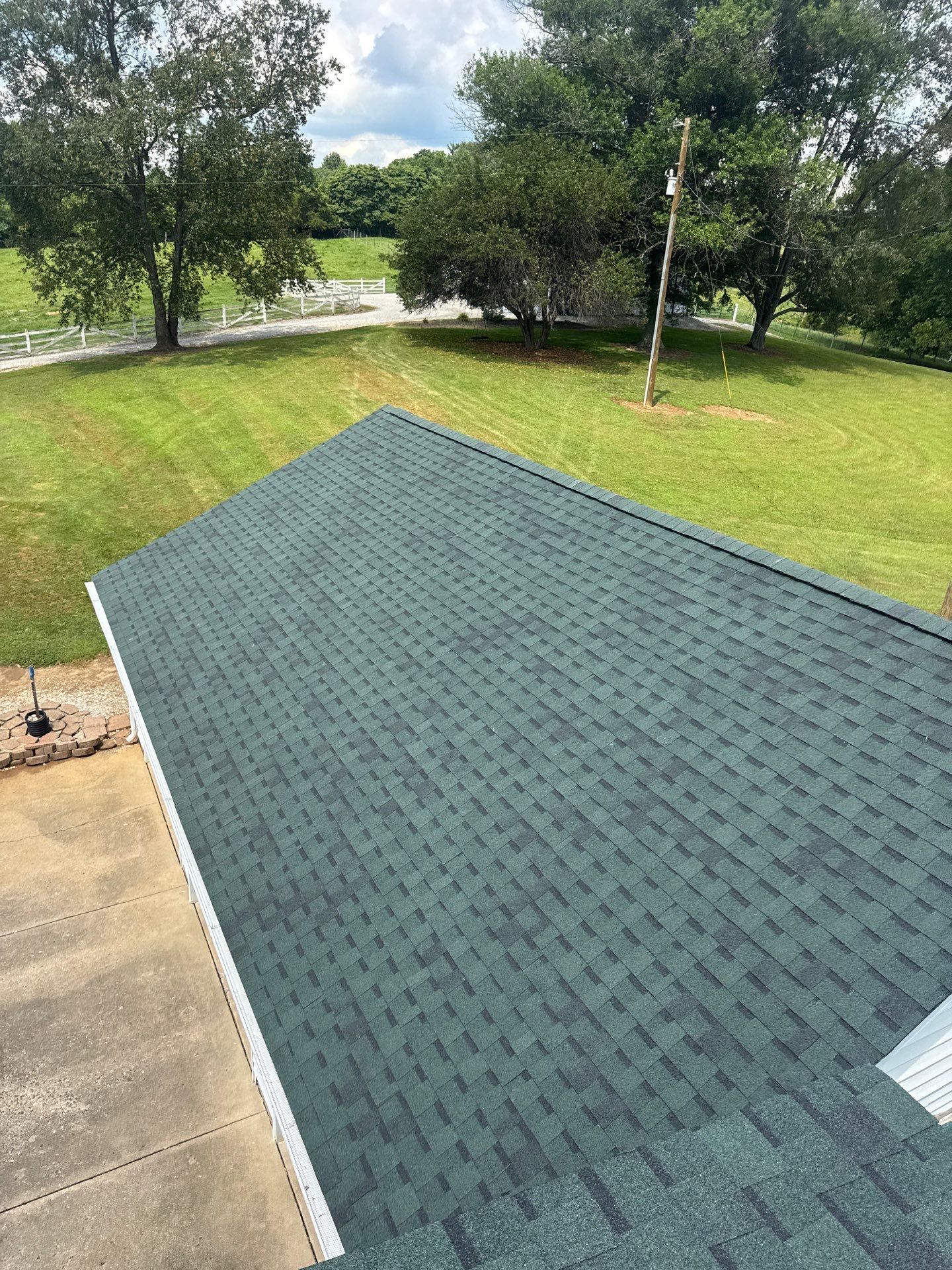 Green shingled roof beside a concrete driveway, with grassy yard and trees in the background.