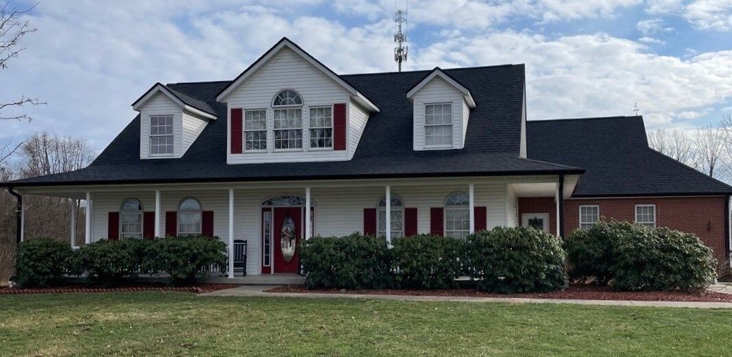 Suburban house with gray siding, red front door, white trim, and brick accents behind a lawn