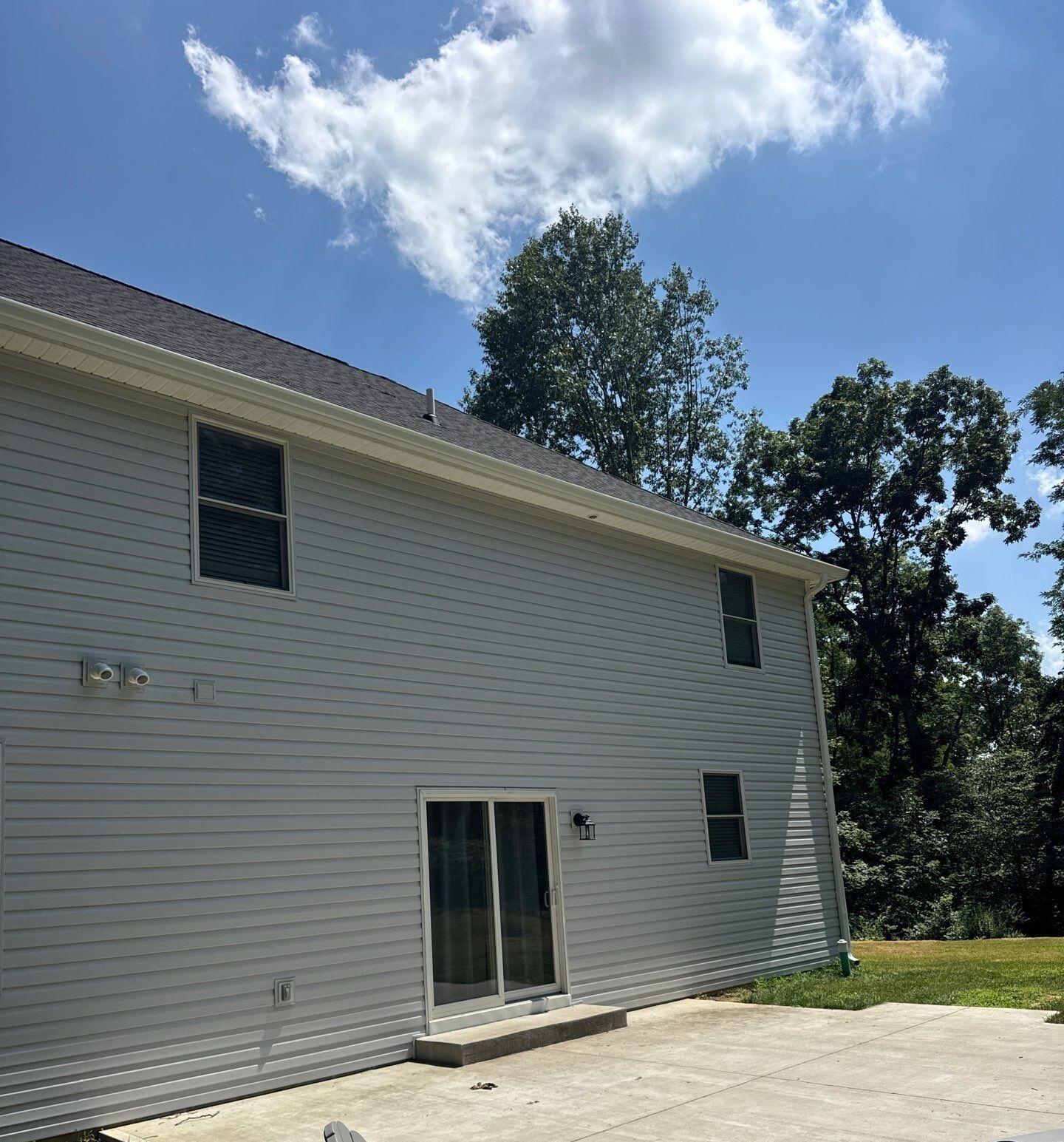 Two-story gray house with white siding, sliding glass door, and concrete patio under a blue sky.