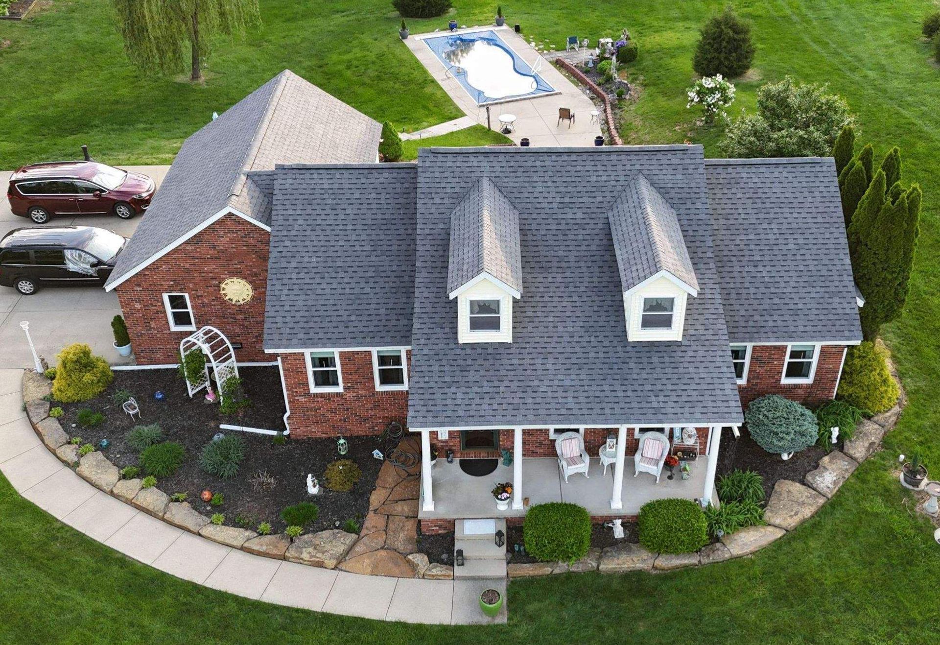 Aerial view of a brick house with a gray roof, porch, curved driveway, and backyard pool.