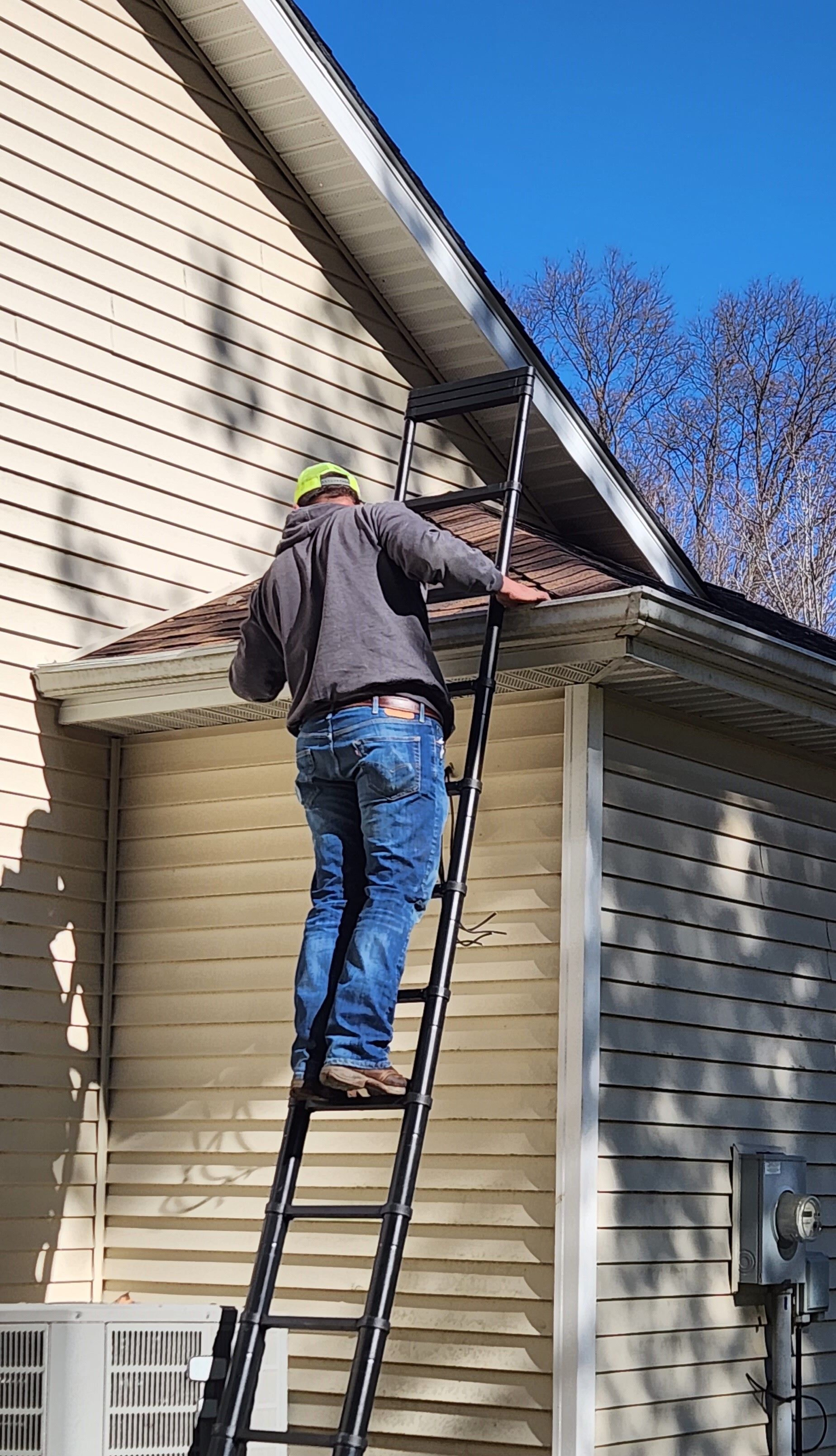 Worker on a ladder inspecting or repairing the roof edge of a beige house.