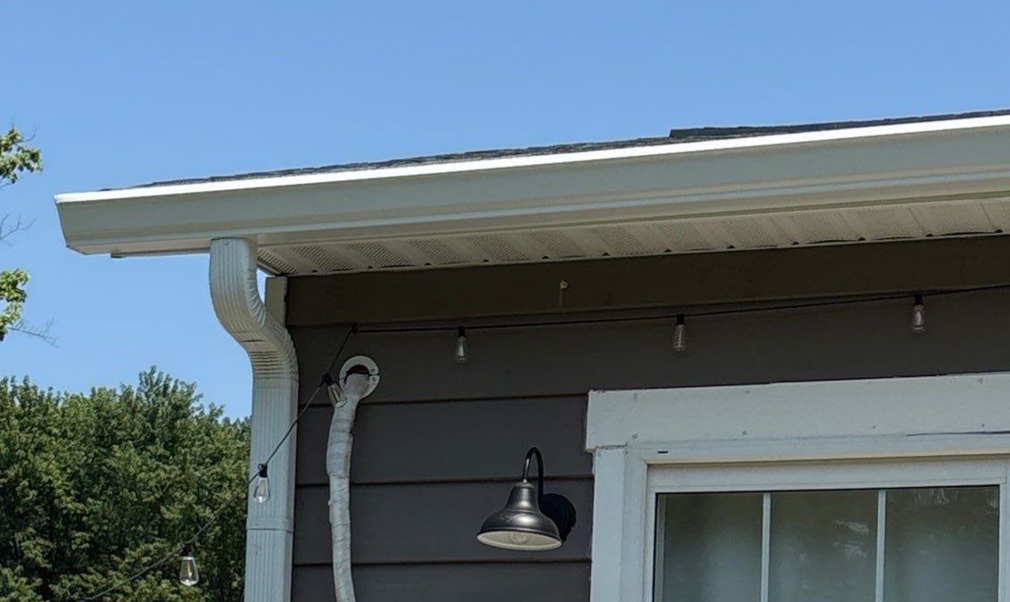 White house eave with gutter, outdoor light, and sliding window under gray roof against blue sky