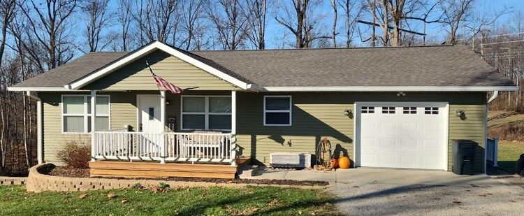 Single-story beige house with front porch, American flag, and attached garage on a sunny day