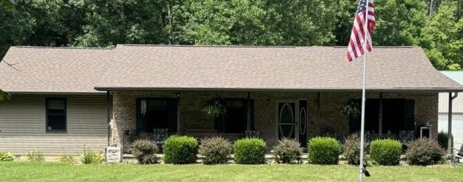 Single-story beige house with a front porch, shrubs, and an American flag in the yard.