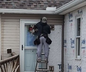 Worker on ladder removing a wreath from a front door of a house under construction