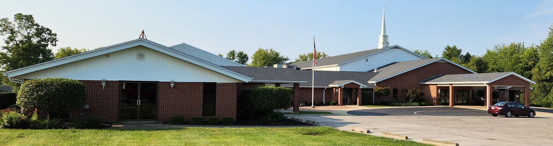 Single-story brick building with a white roof and parking lot in front on a sunny day