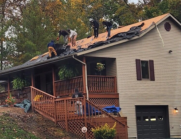 Workers repairing a roof on a beige house, with a porch and garage visible below.