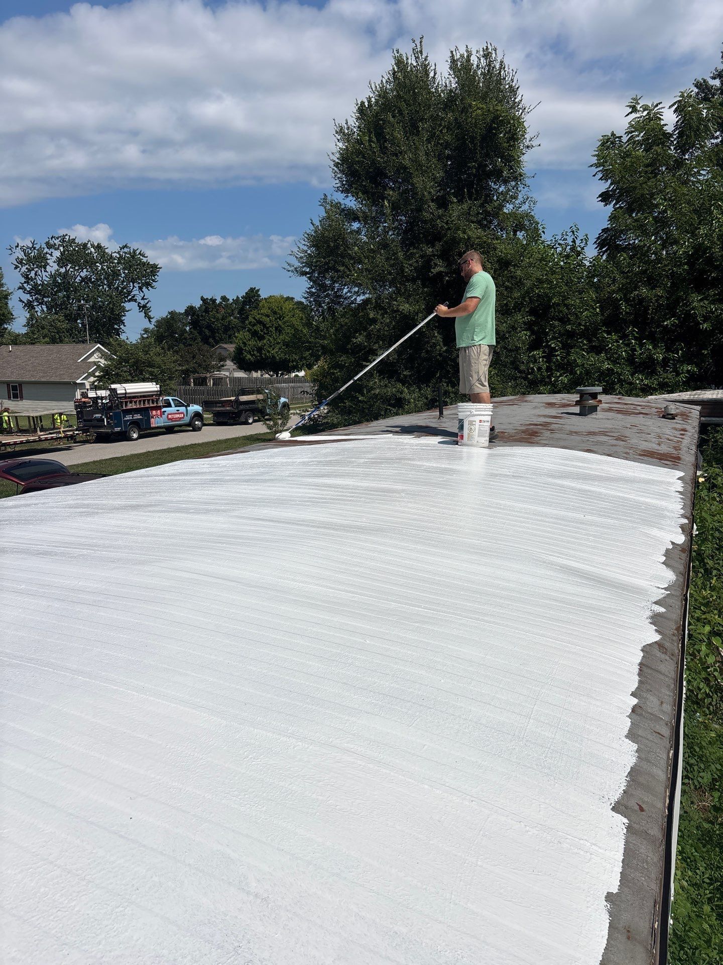Worker spraying white coating on a flat rooftop under a partly cloudy sky