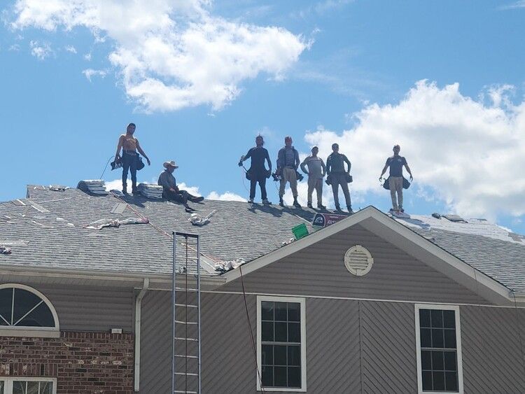 Workers standing on a roof with ladders, inspecting roof damage under a blue sky