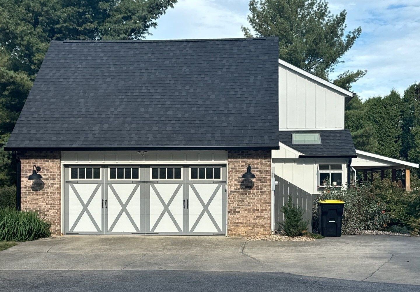 Suburban detached garage with black roof, white trim, brick lower facade, and double barn-style doors
